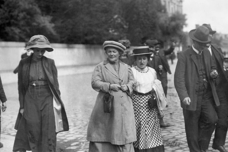 Clara Zetkin and Rosa Luxemburg walking togeher on the street with other women and men around. Black and white photo