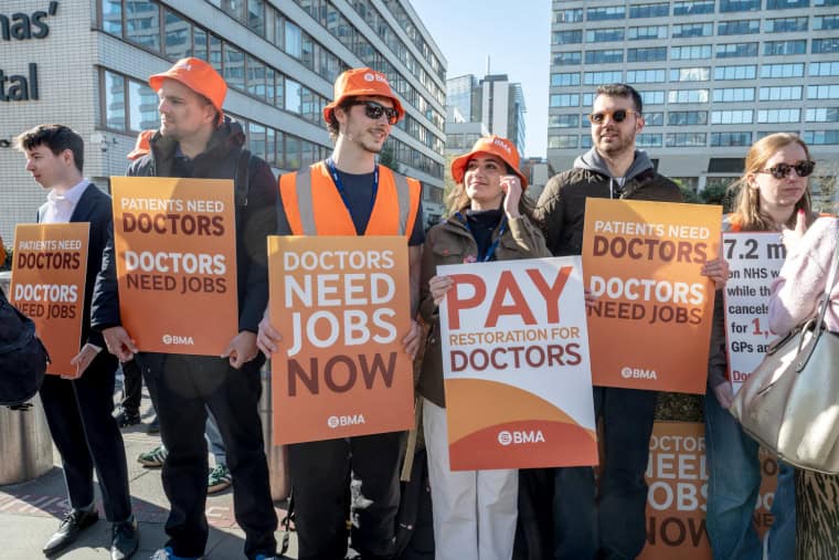 Six resident doctors on strike hold placards up that read 'Pay doctors' and 'Doctors need jobs now'